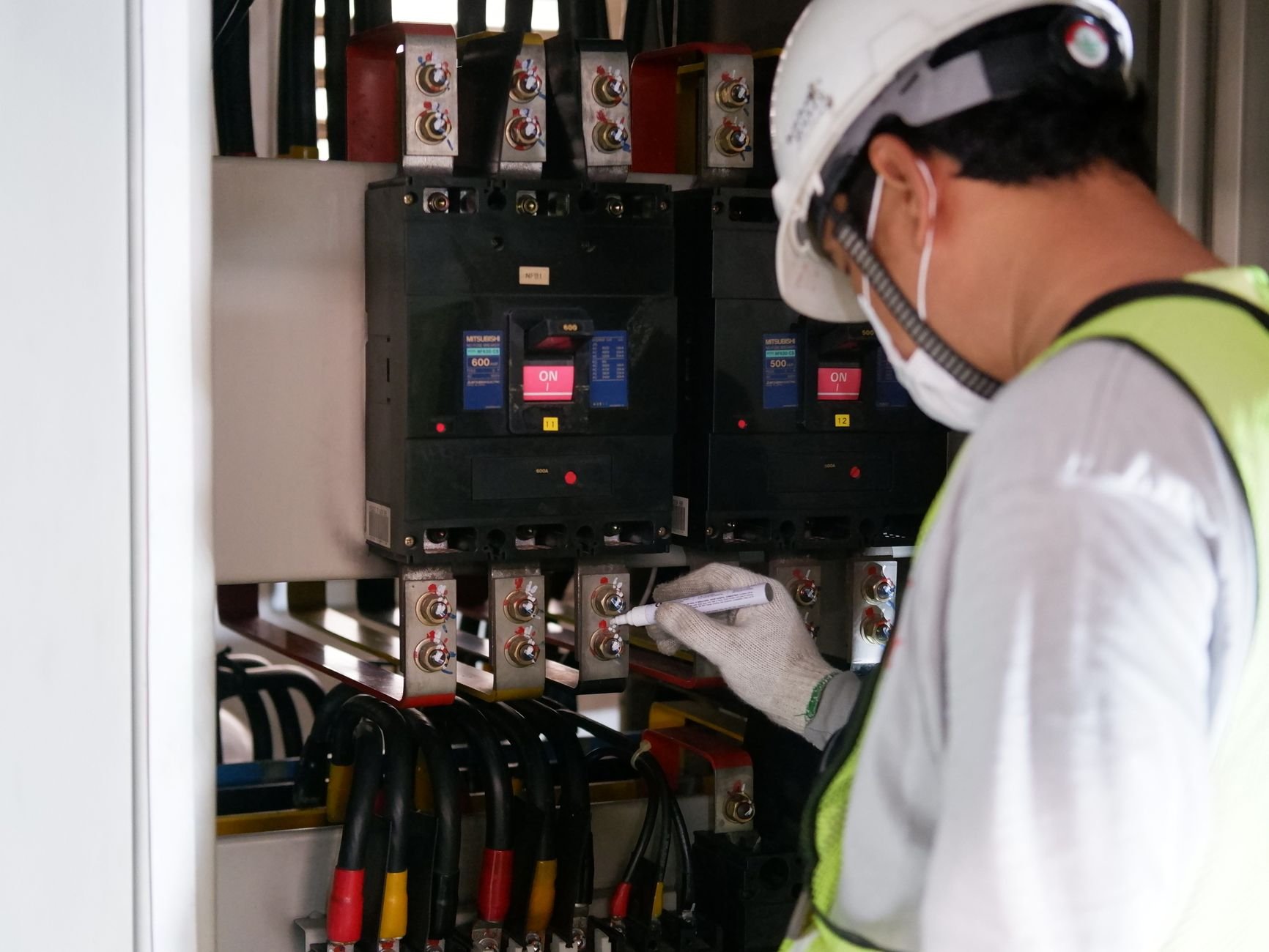 Technician in safety gear inspecting electrical panels in an industrial setting.